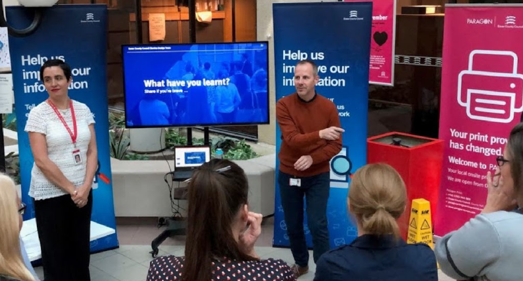 Four women watching a man and a woman present in front of a televion about Learning and Development