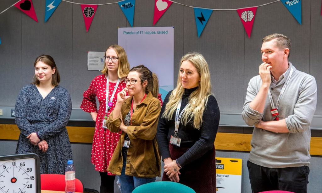 Four women and a man staanding up and listening to a presentation