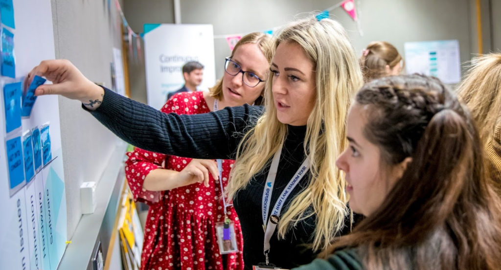 Three women working on a card sorting exercise against a wall.