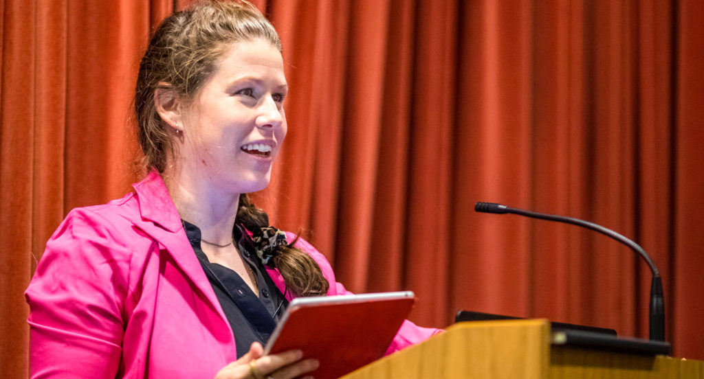 Woman holding an ipad behind a podium giving a talk