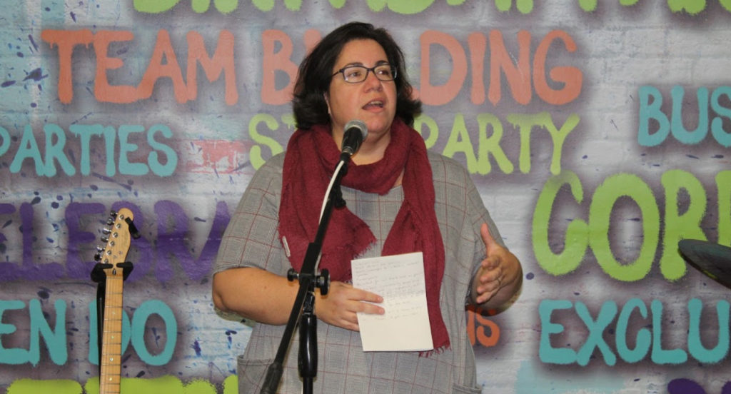 A woman stood being a microphone on a stage giving a talk
